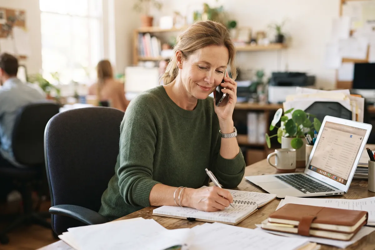 A business owner on a phone call taking notes while reviewing their options